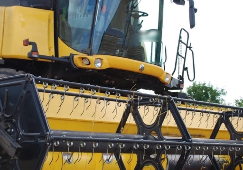 Yellow combine harvester header with its reel tines, parked at the field edge