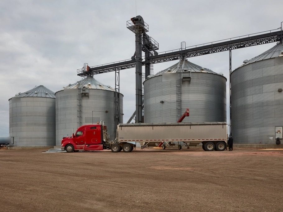 Grain truck loading beside corrugated steel storage bins and an elevator leg